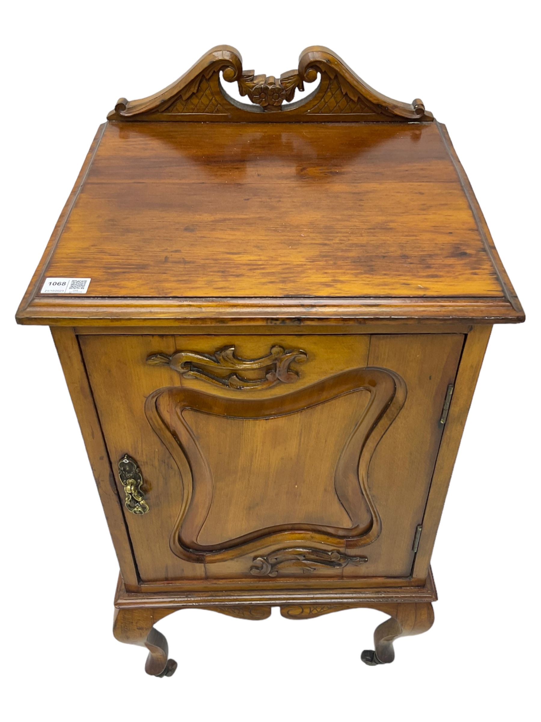 Edwardian Art Nouveau walnut bedside cabinet, raised broken swan neck back with carved flower heads, single fielded panelled door enclosing single shelf, raised on cabriole supports with ceramic castors