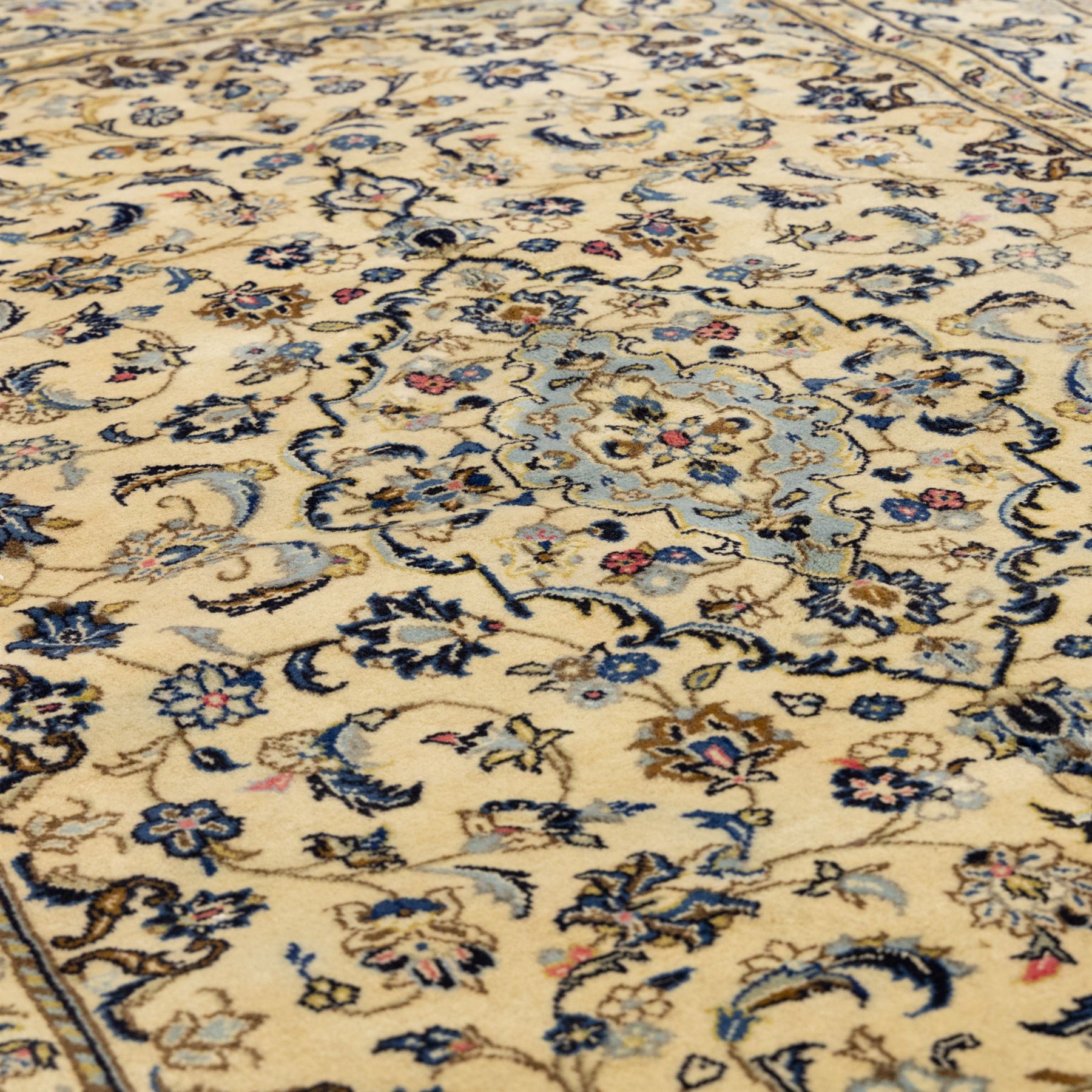 Central Persian Kashan hand-knotted carpet, ivory ground, with a central pale blue shaped floral medallion with pendants, surrounded by scrolling foliate and floral motifs incorporating rosettes, palmettes and delicate vine work in blue, cream and beige tones, enclosed by an ivory border with repeating palmettes and meandering vines, flanked by floral guard stripes, with cotton fringes