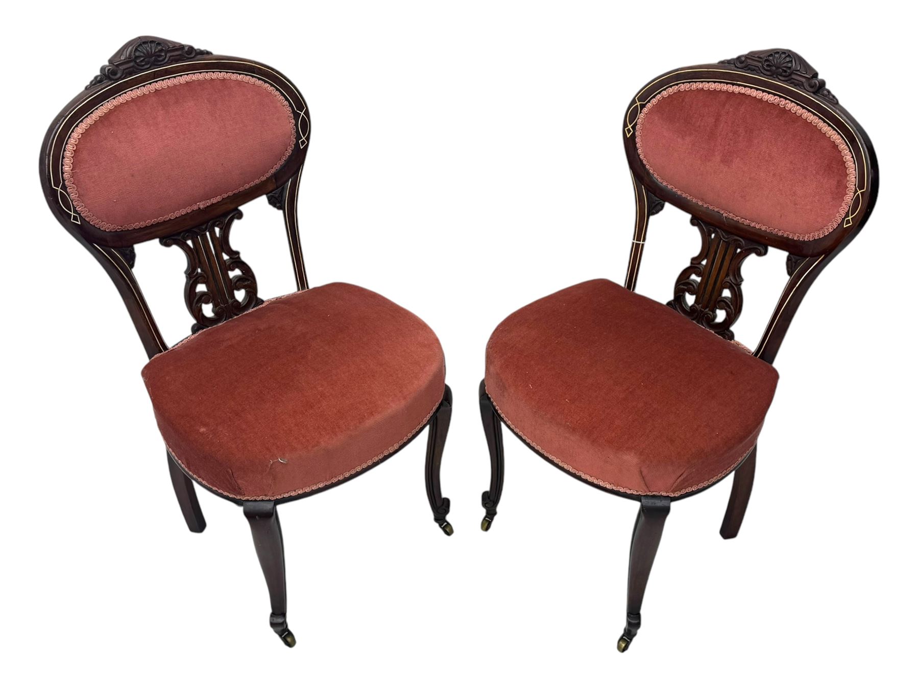 Pair of Edwardian inlaid rosewood salon chairs, upholstered in dusky pink fabric with gimp trim, oval backrest with carved crest rail with central shell motif and pierced splat, on cabriole supports terminating in castors