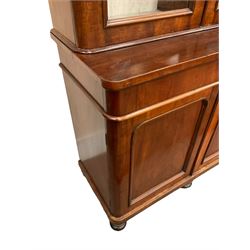 Large Victorian mahogany bookcase on cupboard, projecting cornice over three glazed doors enclosing lined shelves and back, the lower section fitted with three drawers and three panelled cupboards, plinth base on turned feet 