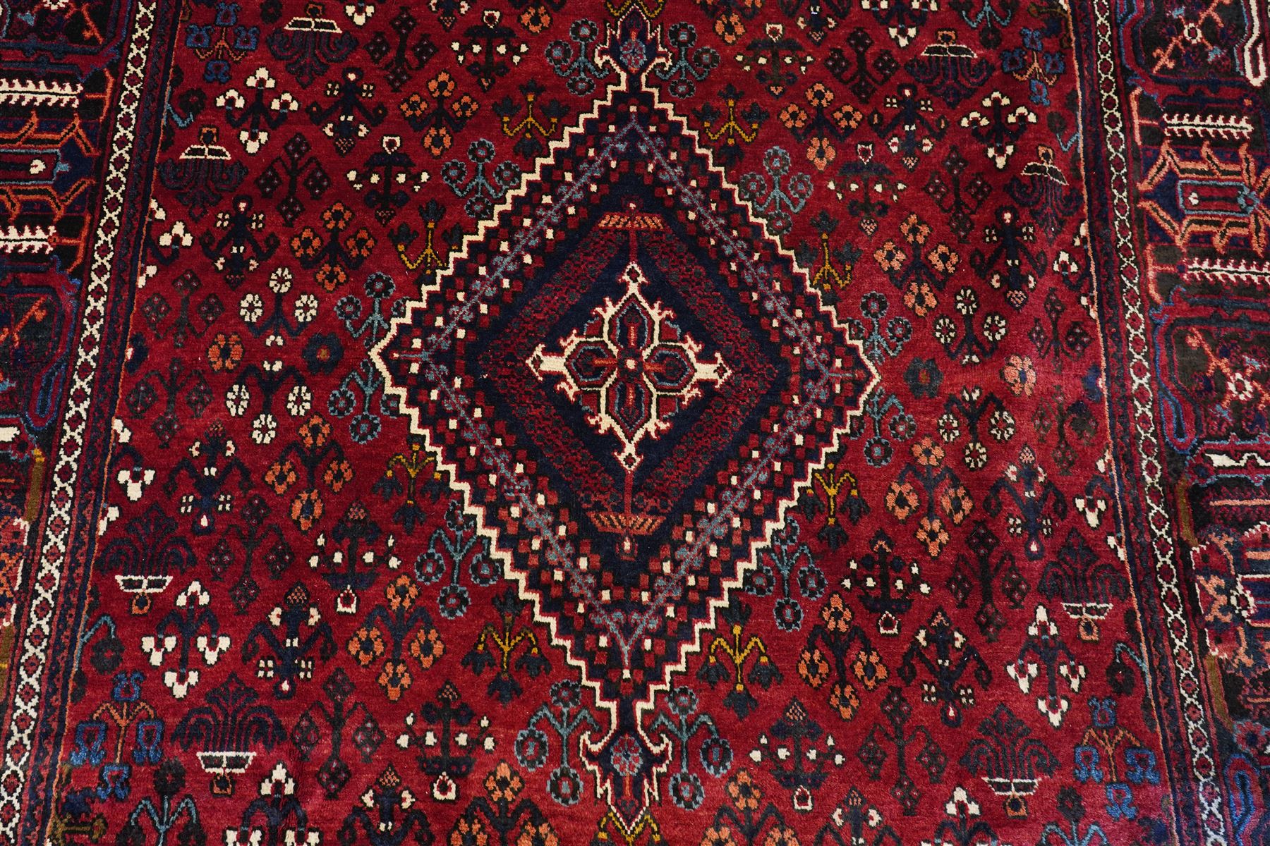 Central Persian Joshaghan hand-knotted carpet, deep red field decorated with a lattice design of stylized boteh and palmette motifs arranged around a stepped diamond medallion, navy corner spandrels similarly decorated enclosed by a dark indigo main border of floral and geometric motifs between multiple guard stripes, with cotton fringe ends 