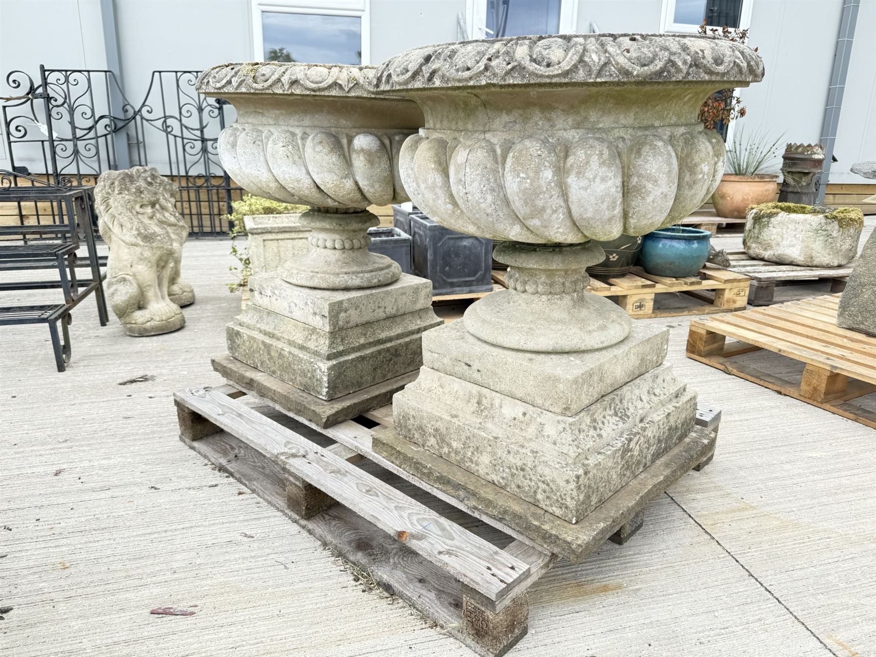 Pair of large weathered Country House Haddonstone garden urns, acanthus carved rim above gadrooned bowl, beaded detailing to the neck, raised on stepped double plinth base
