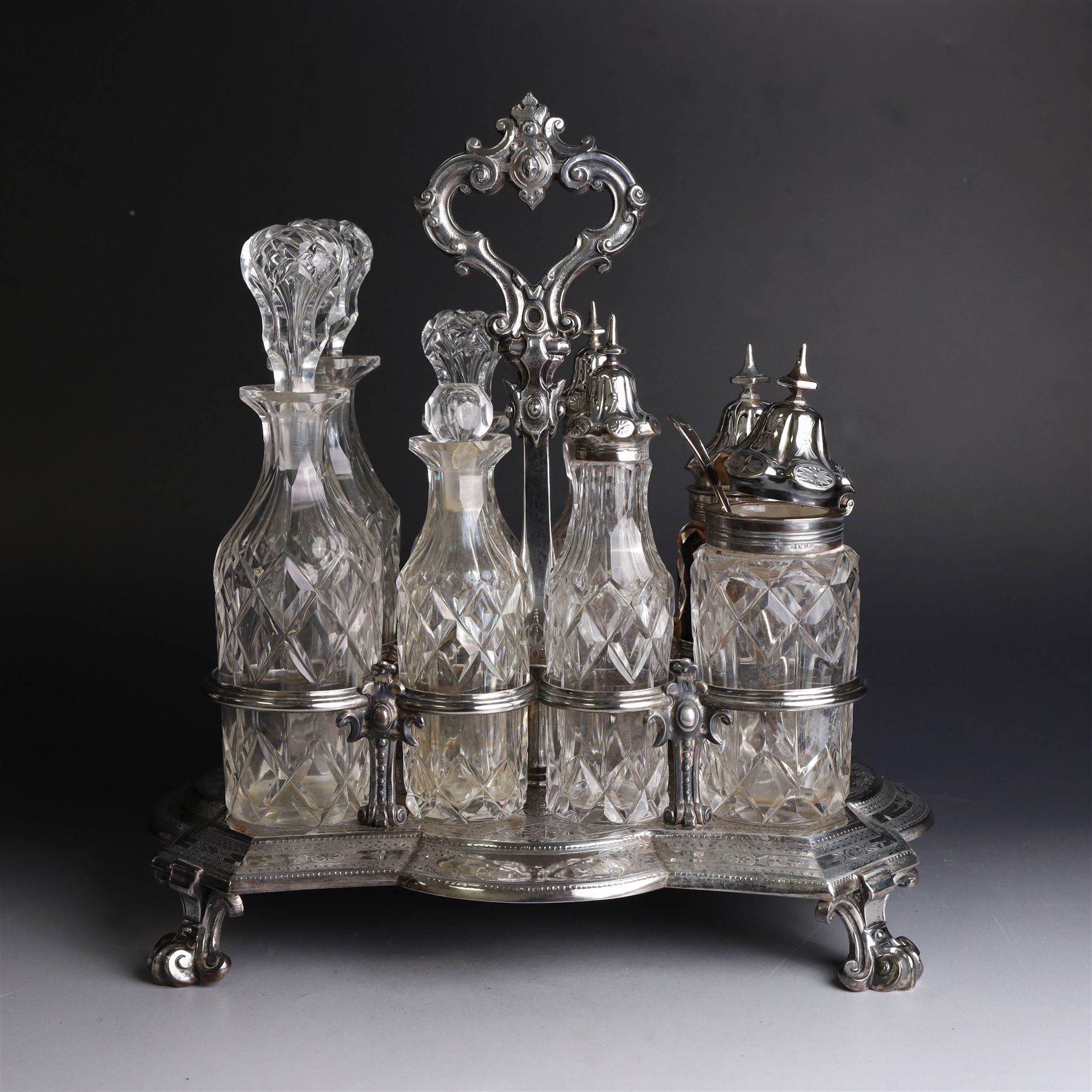 Victorian silver cruet stand, containing eight cut glass cruet bottles, four with silver covers, upon a shaped base with four scroll feet and loop handle, chased with floral and foliate decoration, the stand, base and bottle caps all hallmarked John, Edward, Walter & John Barnard, London 1872, one bottle with a matched silver cruet spoon, stand H30cm