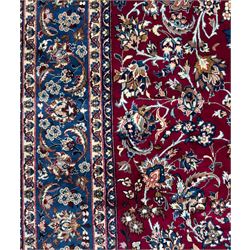 Central Persian Yazd hand-knotted rug, madder red field with scrolling vines, palmettes, and rosettes around a cusped lozenge medallion within a blue ground border of palmettes and flowerheads, 366cm x 250cm