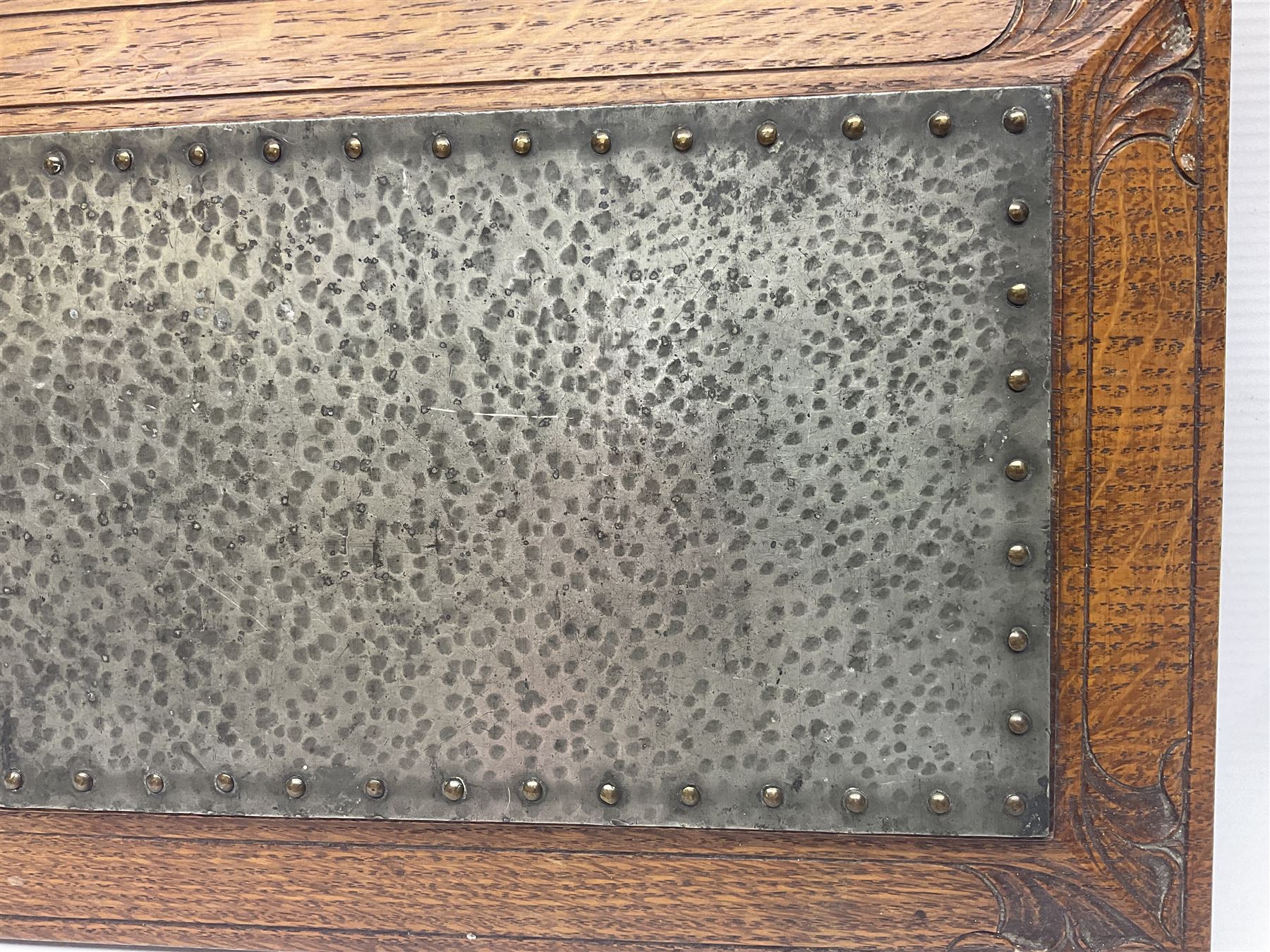 Arts and Crafts oak stand by Arthur Simpson of Kendal, of rectangular form with central hammered pewter panel, surrounded by a border with carved foliate corners, upon two bar supports, bearing label detailed 