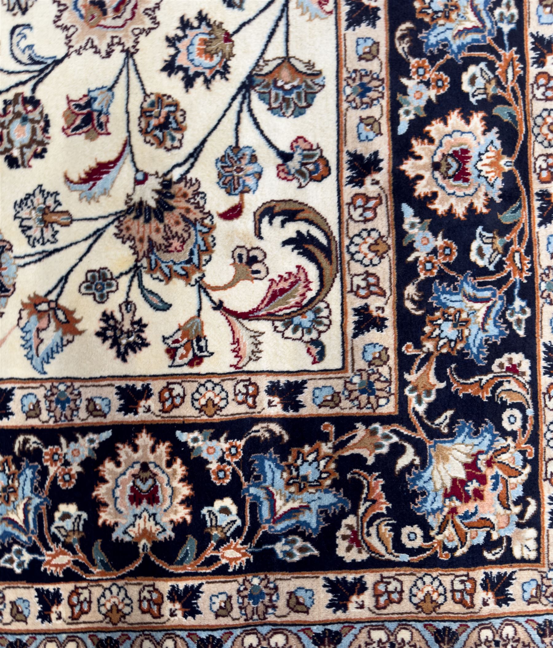 North East Persian Meshed hand-knotted rug, ivory field with scrolling vines, palmettes, and rosettes in shades of blue and brown, within a dark blue border of palmettes and flowerheads between multiple guard stripes, with cotton fringe ends  