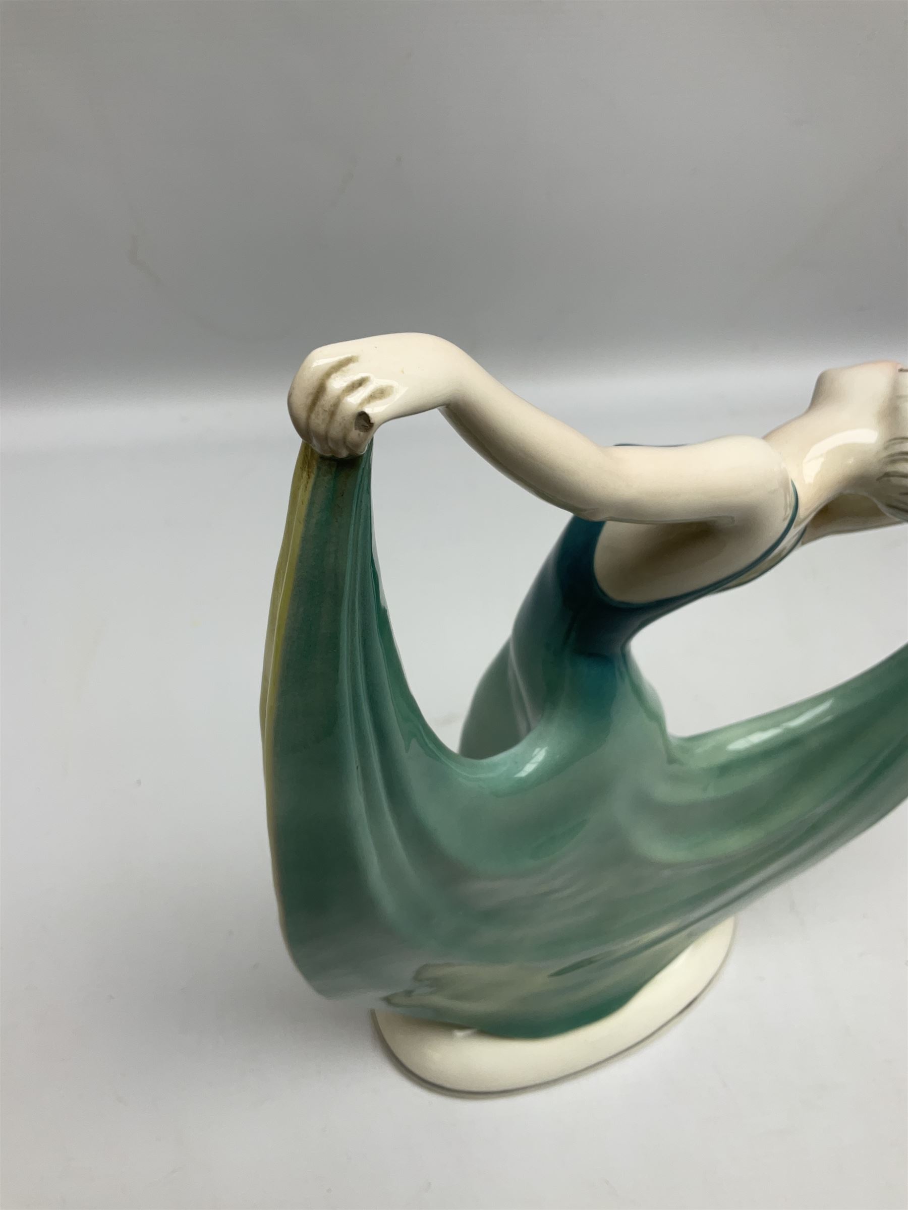 Early 20th century Hertwig Katzhütte figure of an Art Deco lady dancing, wearing a green, blue and yellow dress, stood upon on a domed plinth, with green cat H house printed mark beneath, H32cm