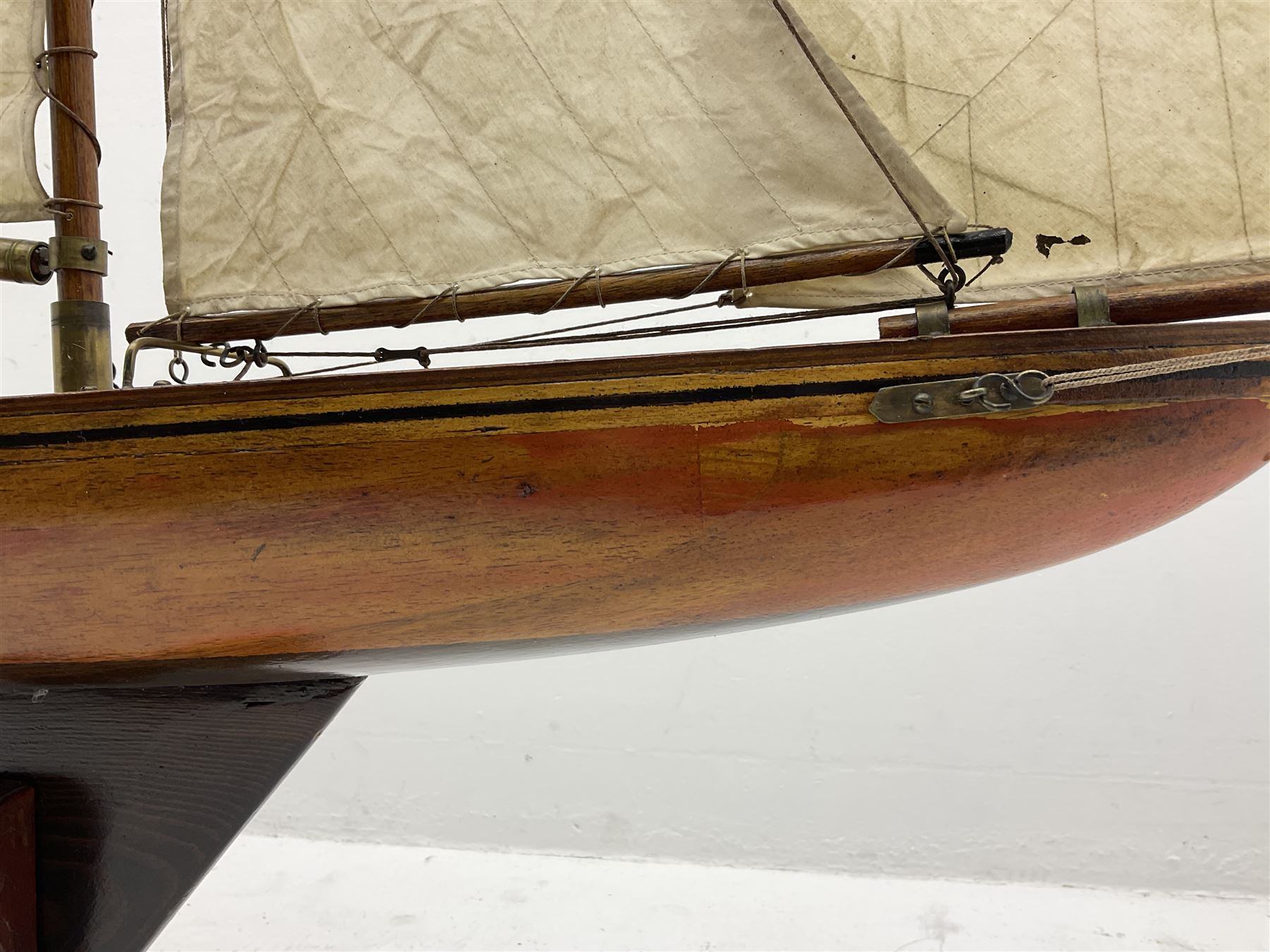 Early 20th century large pond yacht with mahogany hull, stained pine keel with brass rudder, simulated deck hatches and brass fittings, rigged as a staysail schooner (?) with four sails L117cm H148cm; loose mounted on stained pine stand