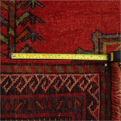 North East Persian Kurdish hand-knotted carpet, madder red field with three vertical and central stepped octagonal medallions enclosing angular geometric motifs with scattered tribal devices, framed by multiple narrow borders with latch-hook patterns, enclosing a bold main border of repeating geometric motifs, palette with indigo, dark brown and soft green tones, 