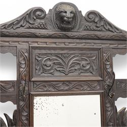Late Victorian heavily carved oak hall stand, the scrollwork pediment with carved lion's head, bevelled mirror plate flanked by carved dragon motifs, over hinged storage compartment and umbrella stands with drip trays, on turned front supports