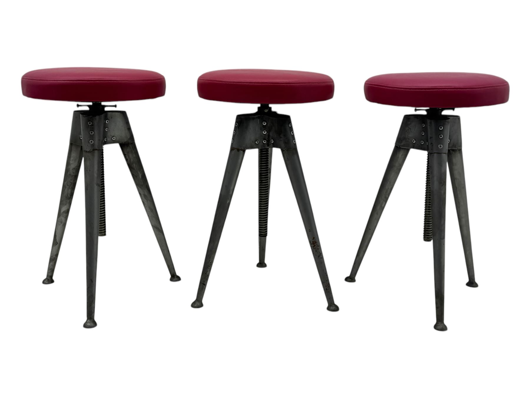 Contemporary industrial design riveted metal table, by repute fashioned from salvaged aeroplane parts, with a circular glass top on a tripod base, accompanied by three adjustable stools upholstered in burgundy