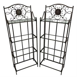 Pair of wrought metal conservatory plant stands, raised back with scrolling design, each fitted with three glass shelves