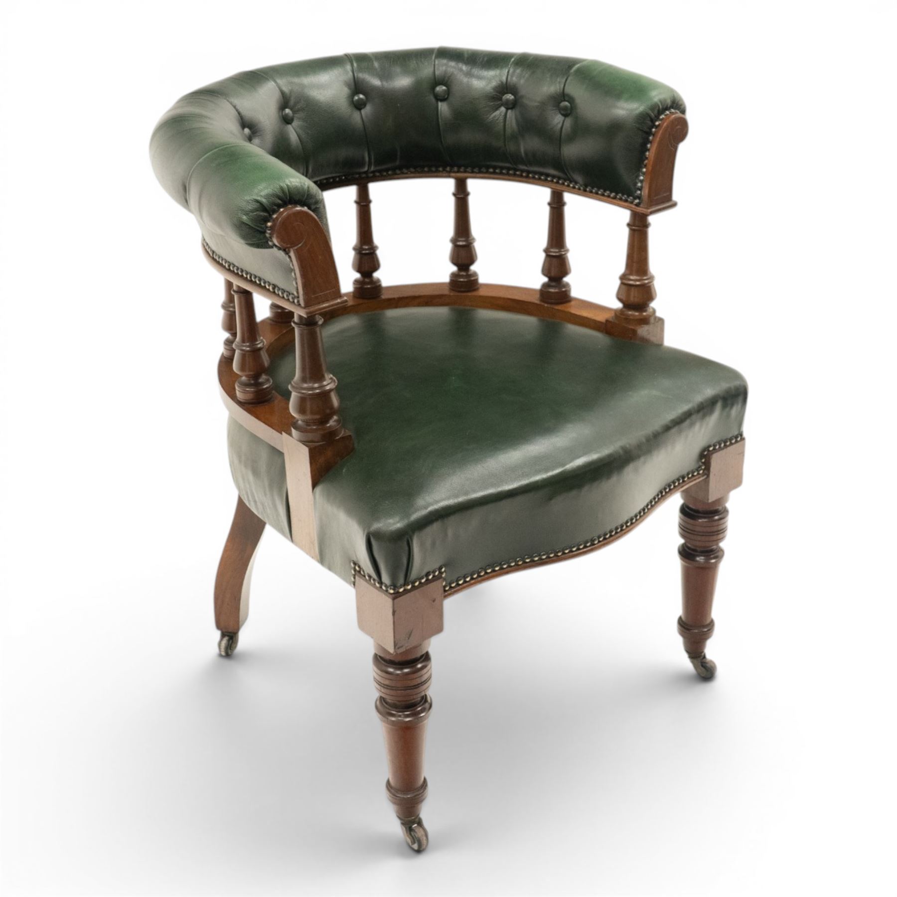 Late Victorian mahogany framed Captains tub desk chair, the green leather upholstered cresting rail over turned spindle supports over a sprung seat, raised on front turned supports terminating to ceramic castors