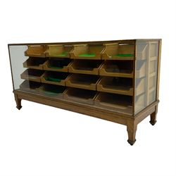 Early 20th century oak framed haberdashery shop counter, glass panel exterior enclosing sixteen graduating drawers with oak fronts and handles, raised on shaped tapering supports 