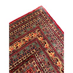 Persian Arak crimson ground carpet, the field decorated profusely with small repeating Boteh motifs, enclosed by multiple border bands decorated with repeating geometric and hook motifs