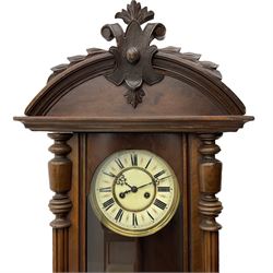 A late 19th century German Wall clock in a mahogany case with a carved semi-circular pediment, fully glazed door with turned side columns and pendant finials, two-part enamel dial with Roman numerals and steel gothic hands, eight-day spring driven movement sounding the hours on a coiled gong, with a wooden pendulum rod and spun brass bob, With key.


