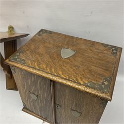 Early 20th century oak smokers cabinet, with brass shield shaped mounts, opening to reveal a compartmentalised interior with three drawers, pipe rack and tobacco jar, together with a small wooden shelf, smokers cabinet H28.5cm