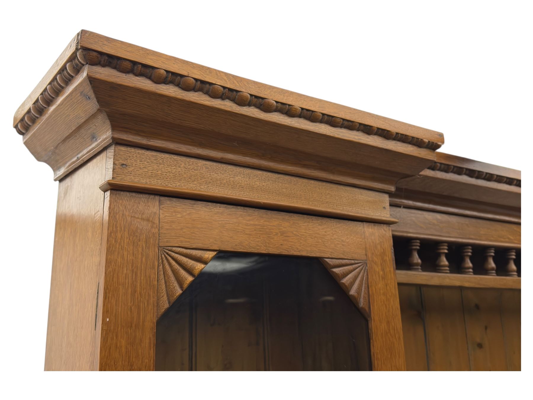 Late 19th century pine dresser, the projecting cornice with dentil and spindle moulded frieze above a three-tier plate shelves, flanked by glazed doors, the base fitted with three frieze drawers over arched apron and carved floral panelled cupboard doors, raised on turned feet