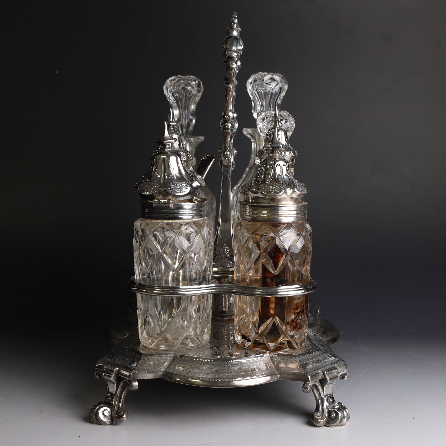 Victorian silver cruet stand, containing eight cut glass cruet bottles, four with silver covers, upon a shaped base with four scroll feet and loop handle, chased with floral and foliate decoration, the stand, base and bottle caps all hallmarked John, Edward, Walter & John Barnard, London 1872, one bottle with a matched silver cruet spoon, stand H30cm