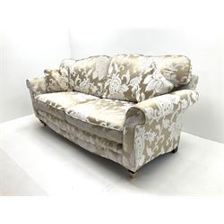 Three seat sofa upholstered in a pale gold ground fabric with floral pattern, shaped cresting rail, scrolling arms