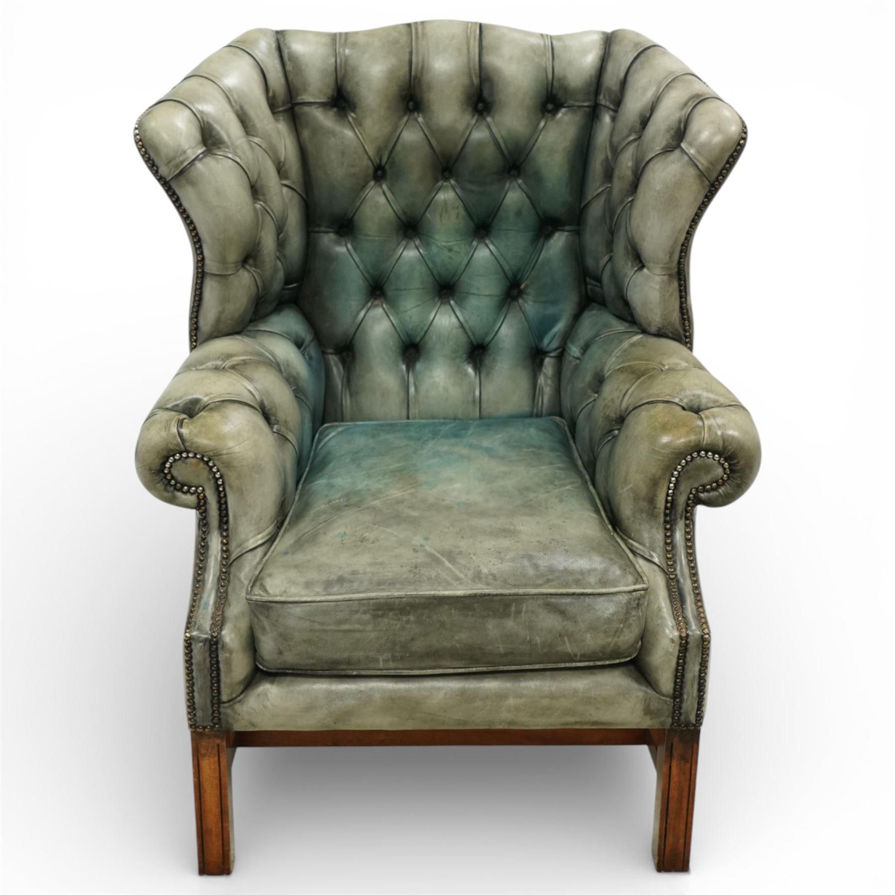 Georgian design mahogany framed wingback armchair, upholstered in rustic pale green buttoned leather with loose seat cushion, raised on square supports united by H-stretcher