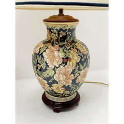 Two Oriental table lamps, each of bulbous form, the first example decorated with pink blossoming flowers upon a dark blue ground, above a fret pattern band, upon a wooden circular stepped base, the second example with white foliate decoration upon a dark blue ground, also with fret pattern band, and upon a wooden circular stepped base, each with fabric shade, including shade each approximately 74cm. 
