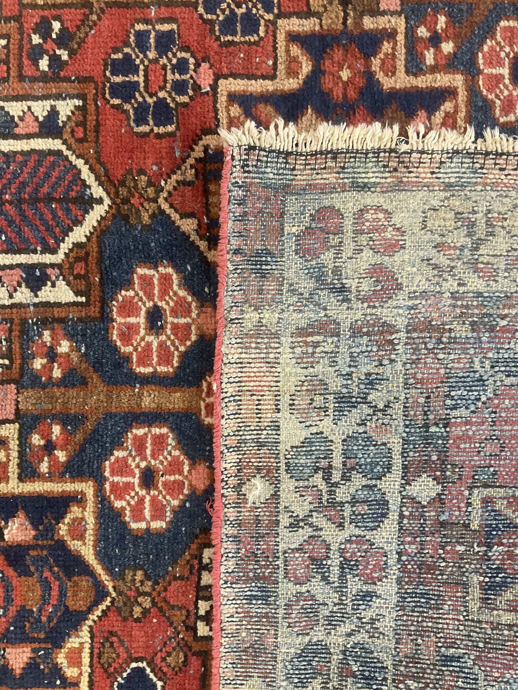 Persian crimson ground rug, the field decorated with three rows of stylised plant medallions and small flowerhead motifs, repeating floral design border with guards 