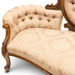 Victorian carved walnut framed double-ended settee with serpentine front, the central oval cameo back with flowerhead carved cresting rail, flanked by foliate C-scroll spandrels, the scroll carved arm terminals over floral carved cabriole supports with scroll feet and ceramic castors, the buttoned back and sprung seat upholstered in pale pink foliate patterned damask fabric