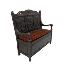 Late 19th century oak settle bench, shaped cresting rail carved with ribbon over triple panelled back, the panels relief carved with scrolled and floral urns and cartouche, hinged box seat, turned front feet, with upholstered squab cushion