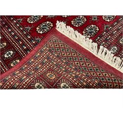 Pakistani Bokhara red ground rug, the field decorated with repeating Gul motifs and lozenges, the multi-band border with stylised plant motifs with dark indigo outlines