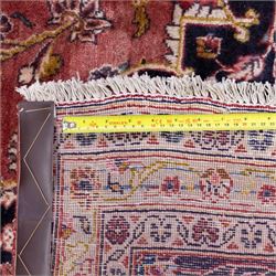 Large Central Persian Kashan hand-knotted carpet, madder red field with central cusped medallion on beige ground enclosed by indigo border with an intricate all-over arrangement of scrolling vines and floral motifs within conforming spandrels and a indigo ground main border ornamented with floral designs, enclosed by guard stripes and cotton fringe ends 