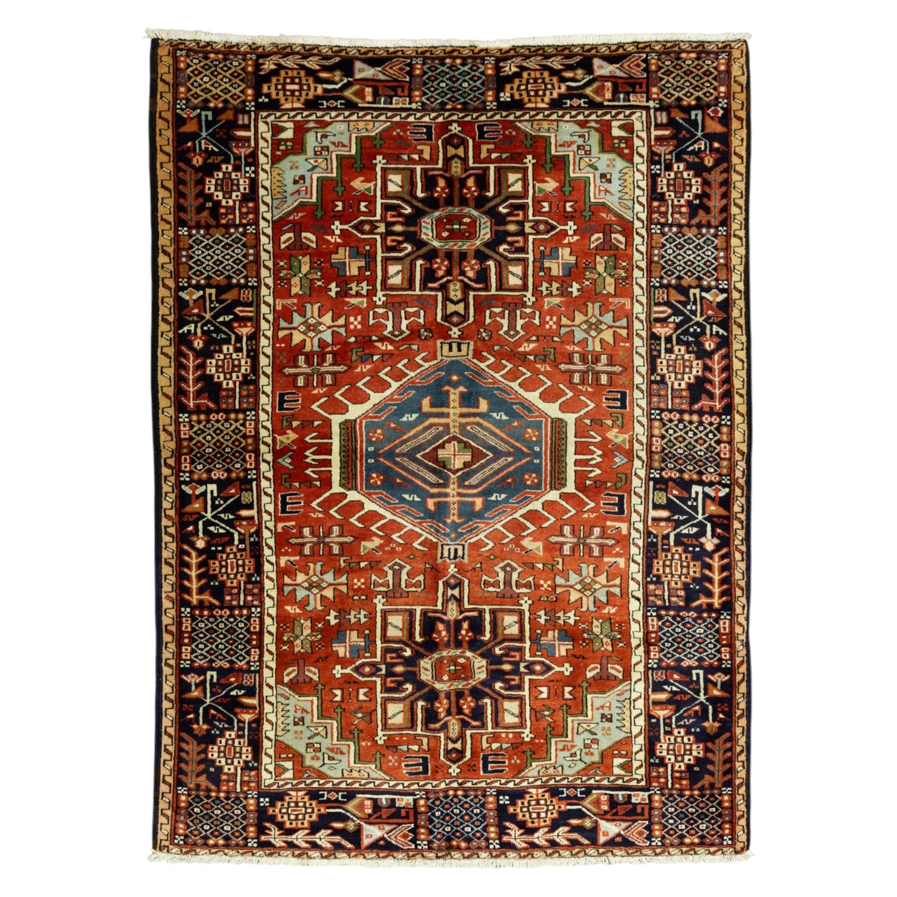 North West Persian Karajeh hand-knotted rug, terracotta ground, with a stepped geometric pole medallion design in blue, ivory and dark navy tones, surrounded by angular tribal motifs incorporating stylised flowerheads, hooked devices and geometric vine work, enclosed by a dark navy border with repeating rosettes and angular leaf motifs, flanked by narrow patterned guard stripes, with cotton fringes