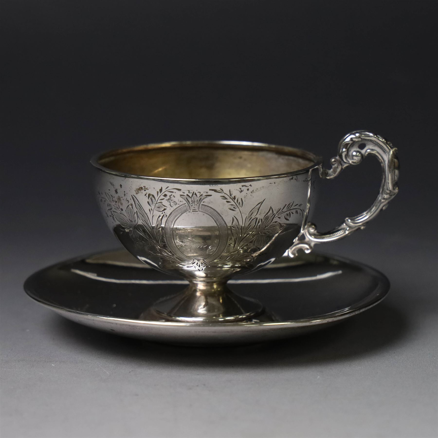 German silver cup and saucer, both with engraved foliate decoration, stamped 800, the saucer with crescent and crown mark
