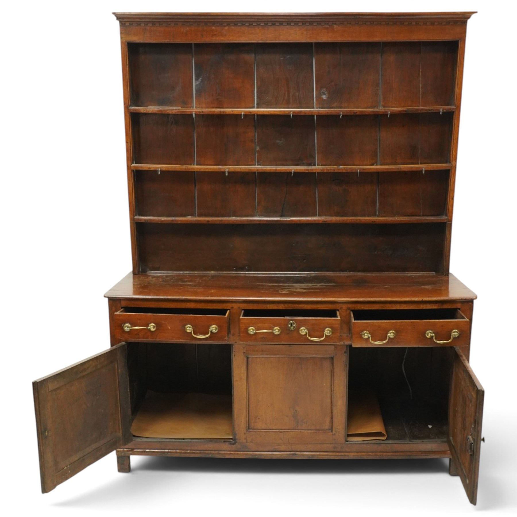 18th century oak dresser with rack, the three-tier plate rack with dentil-carved cornice, the plate shelves with moulded edge and wrought metal hooks, the base fitted with three drawers with brass swan-neck handles over three panelled cupboards, lower moulded edge on stile supports