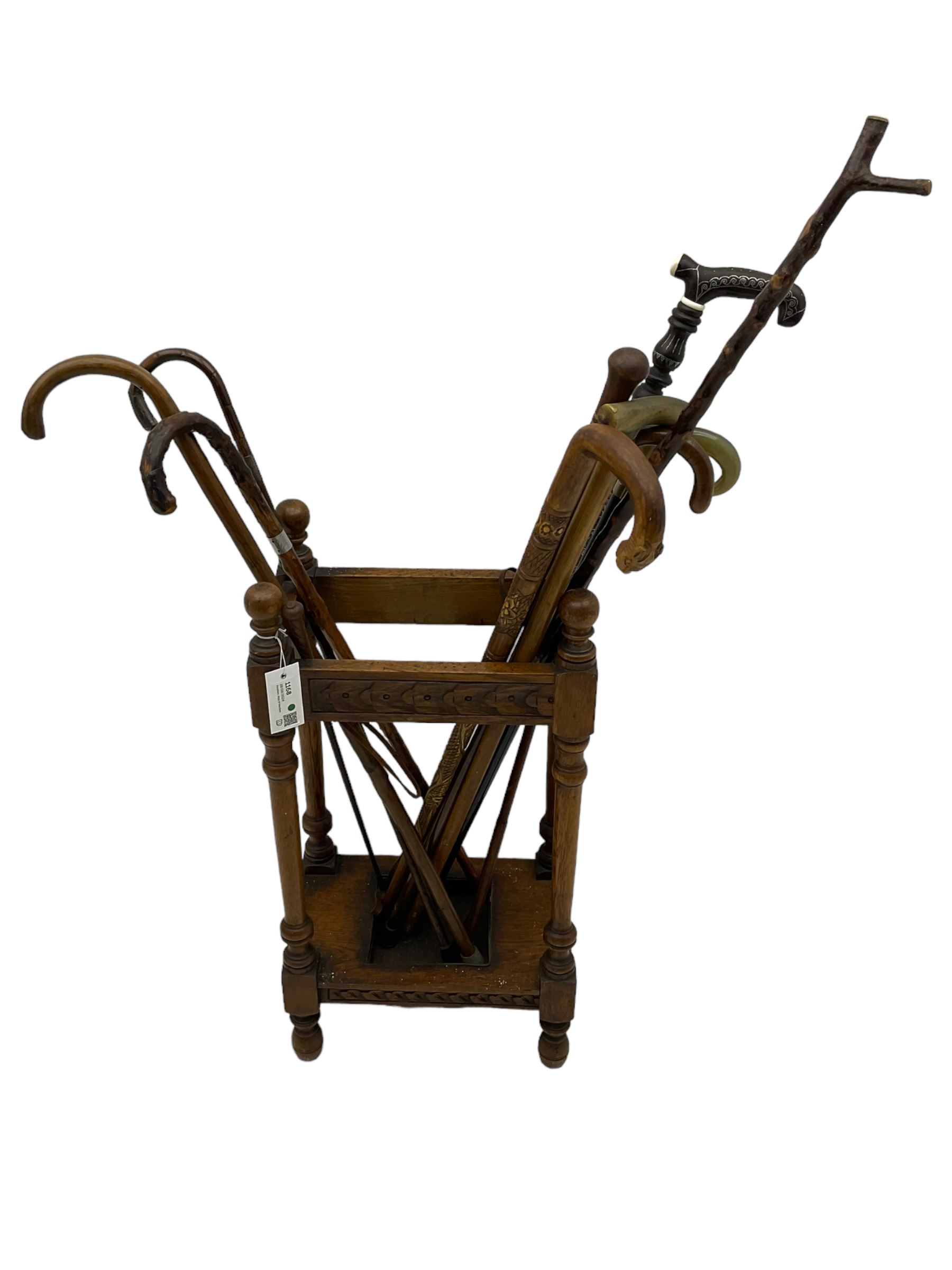 Early 20th century oak stick stand, rectangular structure with decorative carving, square base fitted with tray, on turned supports topped with finials; twelve assorted walking canes 