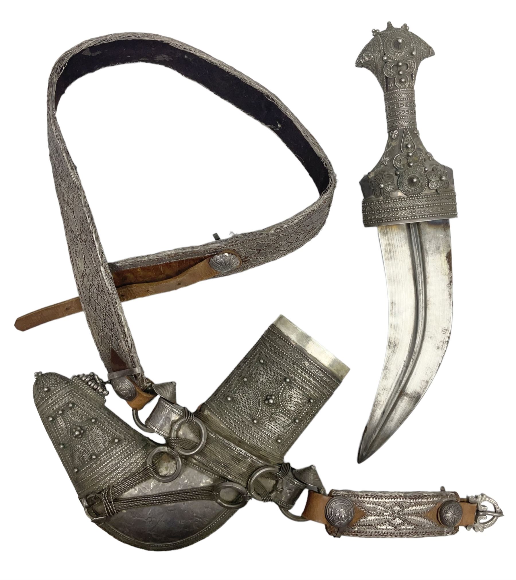 Omani Khanjar dagger, the 19cm curved blade with pronounced medial rib to either side, waisted hilt with dome shaped pommel and silver covered horn grip decorated with filigree bands, floral motifs and beadwork; in an intricately filigree decorated silver and leather scabbard with silver rings woven into the belt mount and fitted with original silver thread-work belt L34cm overall belt length 94cm