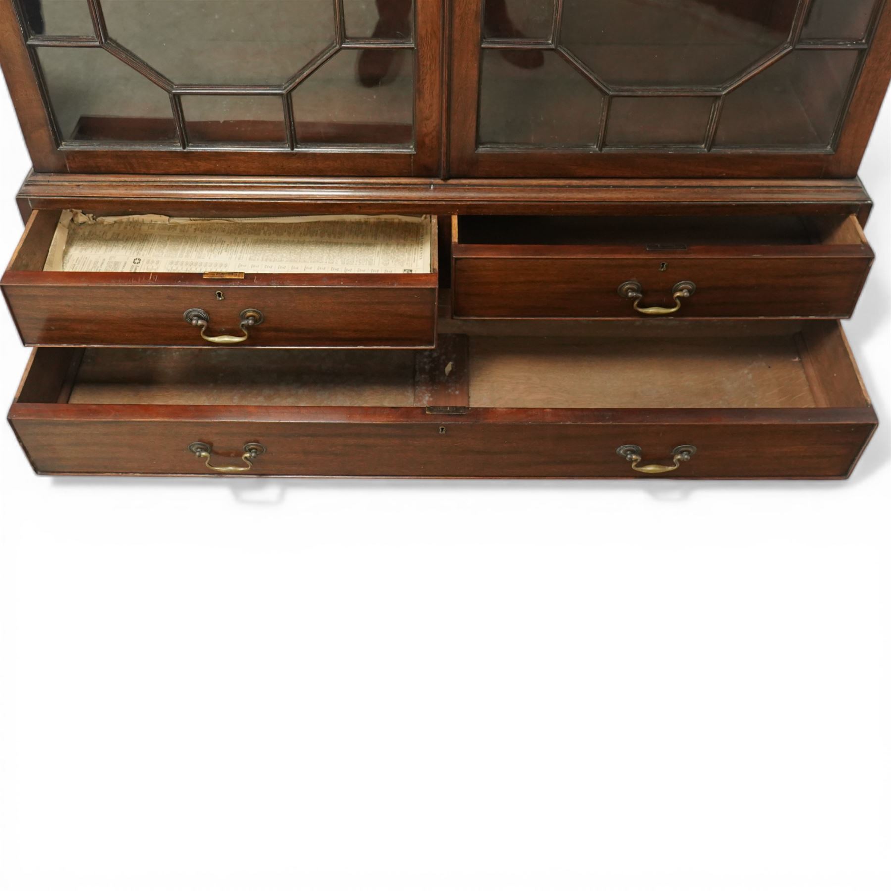 Early 20th century mahogany glazed bookcase, the moulded cornice above a carved frieze with interlaced ornament, enclosed by a pair of astragal glazed doors with geometric glazing bars, the base fitted with two short over two long drawers with brass swan neck handles, raised on bracket feet