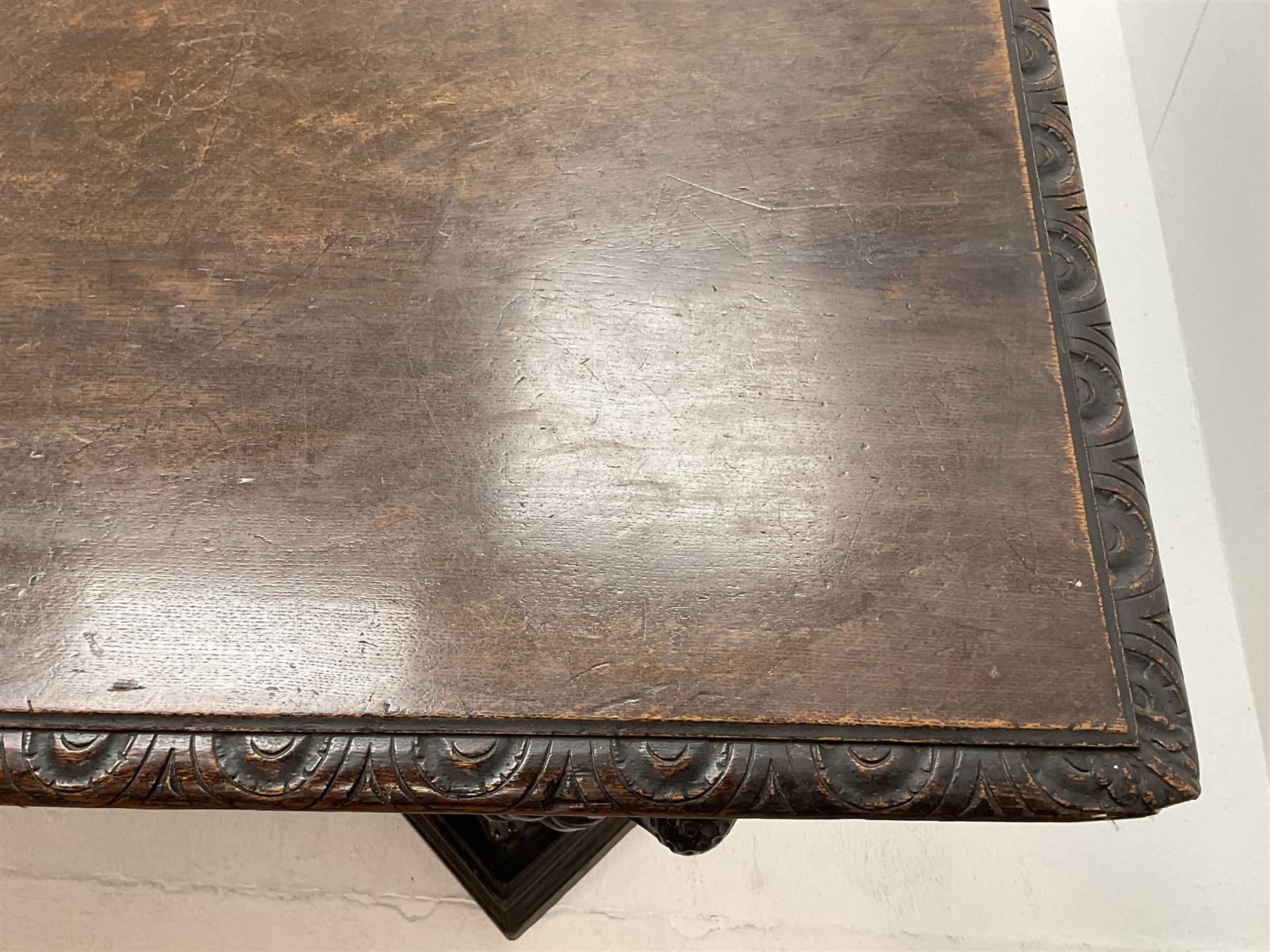 Large 19th century carved oak library table, the rectangular top with lunette carved edge over cartouche panelled and carved  scroll frieze, the central tapering rectangular support relief carved with masks and garlands, on four carved seated lion supports at each corner, on flat angular stretcher with recessed castors stamped ‘Bartholomew & Fletcher, London’