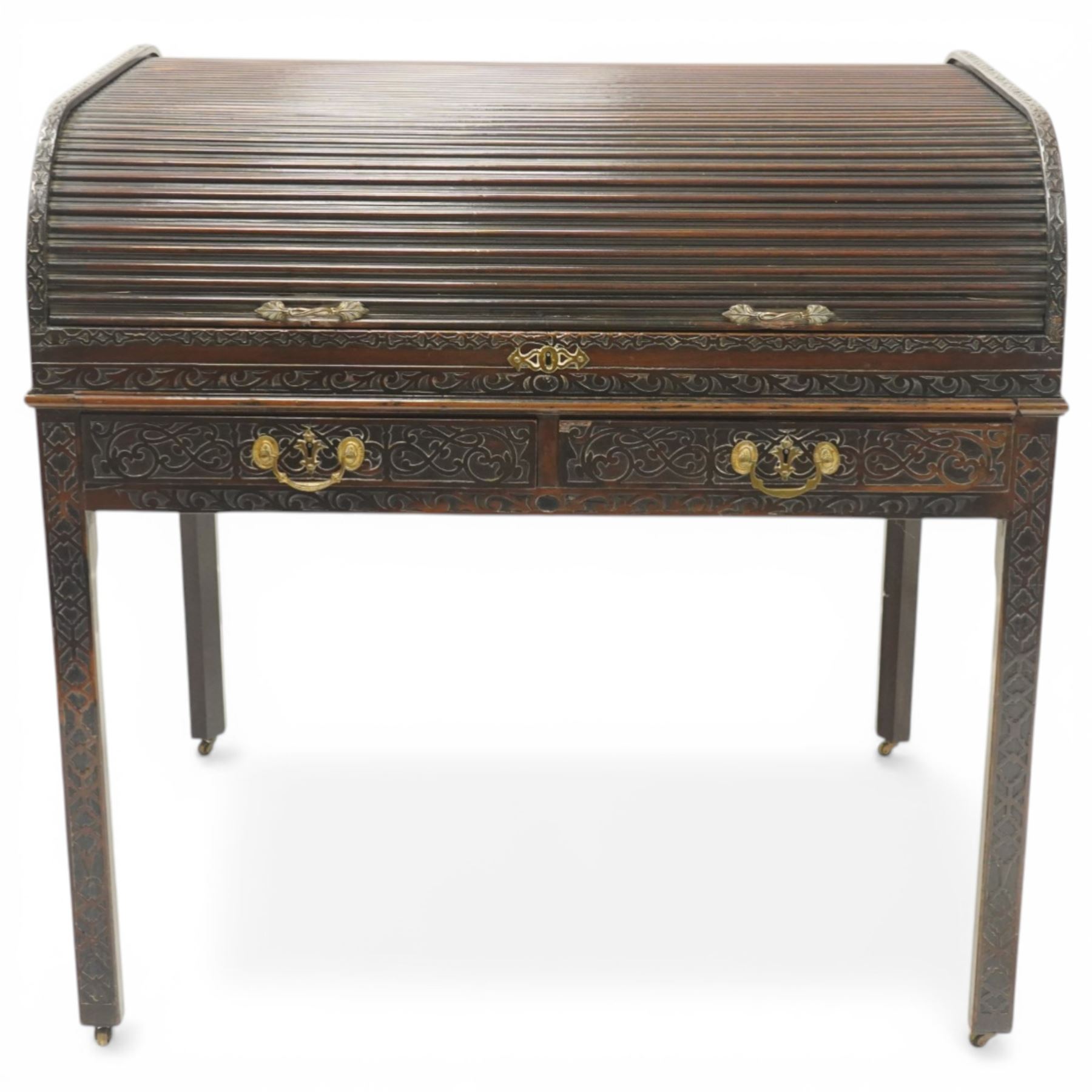 Late 18th century George III mahogany Chippendale design cylindrical roll-top desk carved profusely with geometric and foliate blind-fretwork throughout, the tambour-roll top opening to reveal pigeon holes over an inset red leather writing surface, fitted with two frieze drawers below, raised on square supports with inner chamfer terminating to brass castors, circa 1780s