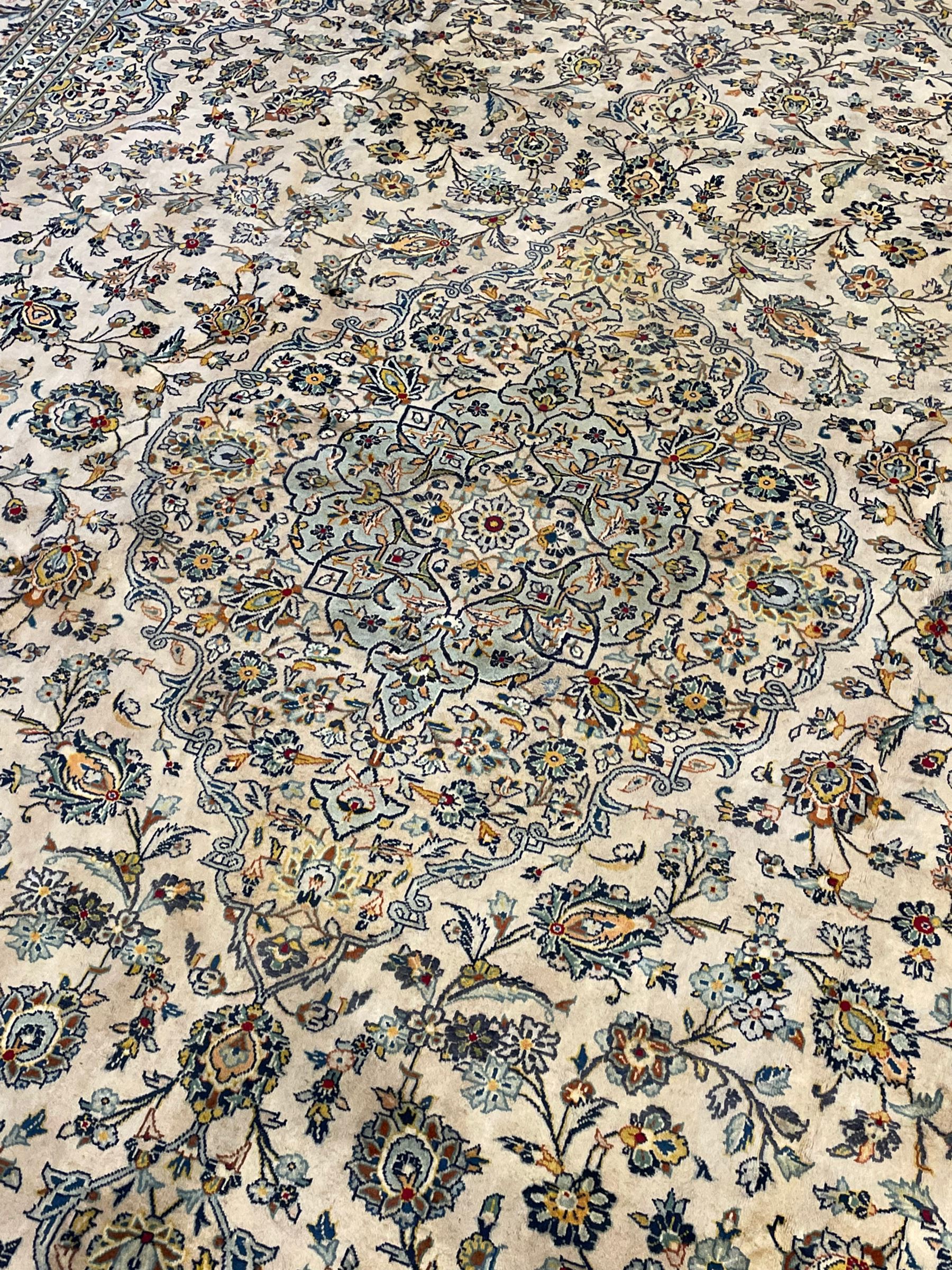 Central Persian Kashan pale khaki ground carpet, shaped central medallion enclosing small stylised motifs, the field decorated profusely with trailing foliate branches and plant motifs, guarded border with repeating floral design 