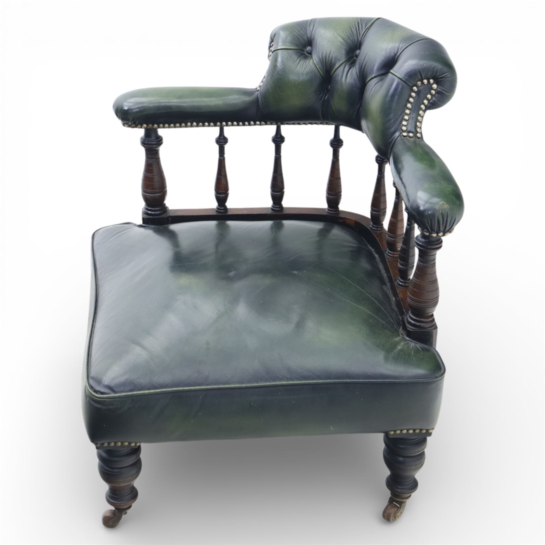 19th century green leather upholstered corner chair, with deep buttoned back and swept padded arms with close studded borders, raised on turned supports united by turned spindles, terminating in brass castors