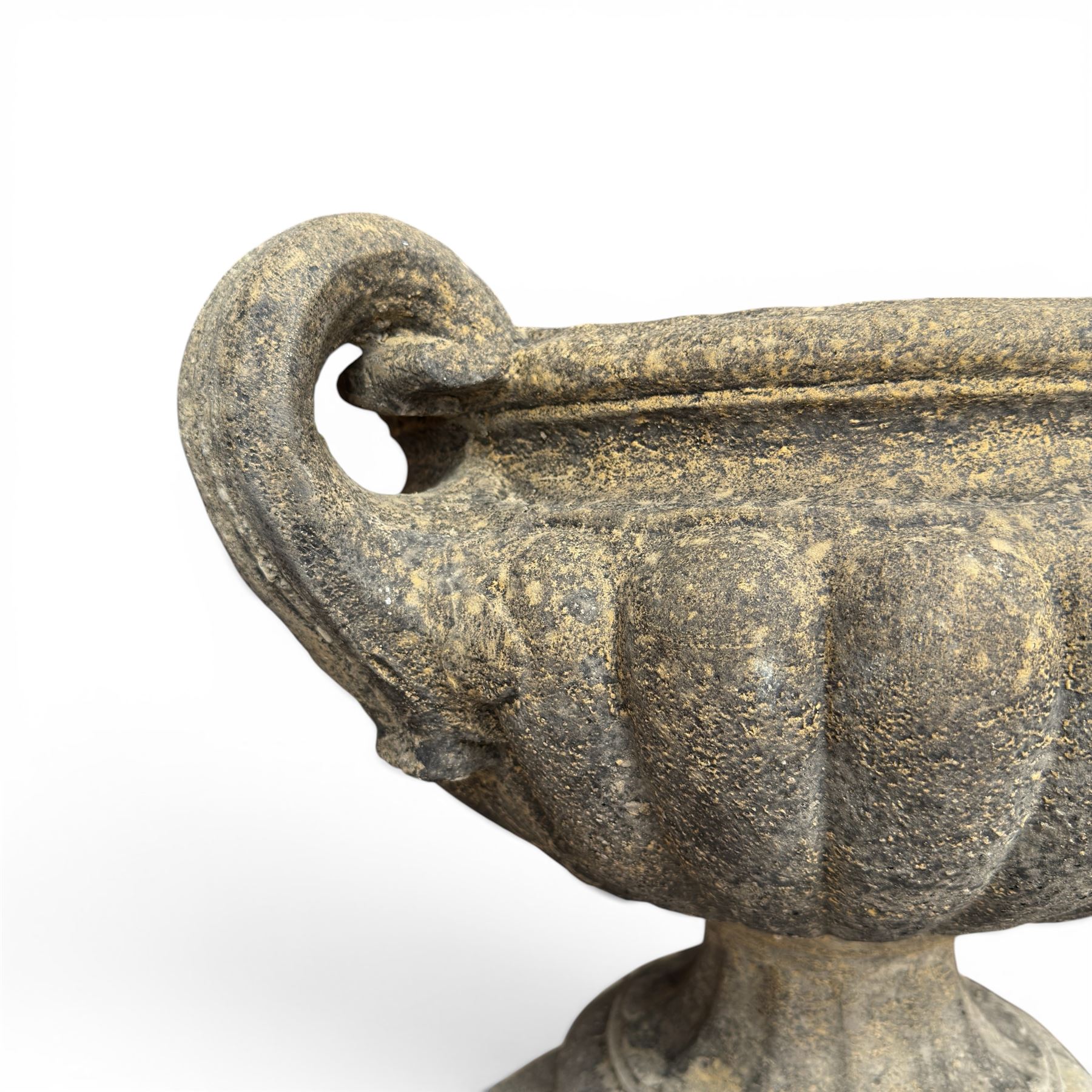 Pair of Neoclassical design weathered cast stone garden urns of kylix form, the rolled rim flanked by twin pierced scroll handles over a shallow gadrooned bowl, raised on a fluted circular socle and faux panelled square pedestal base