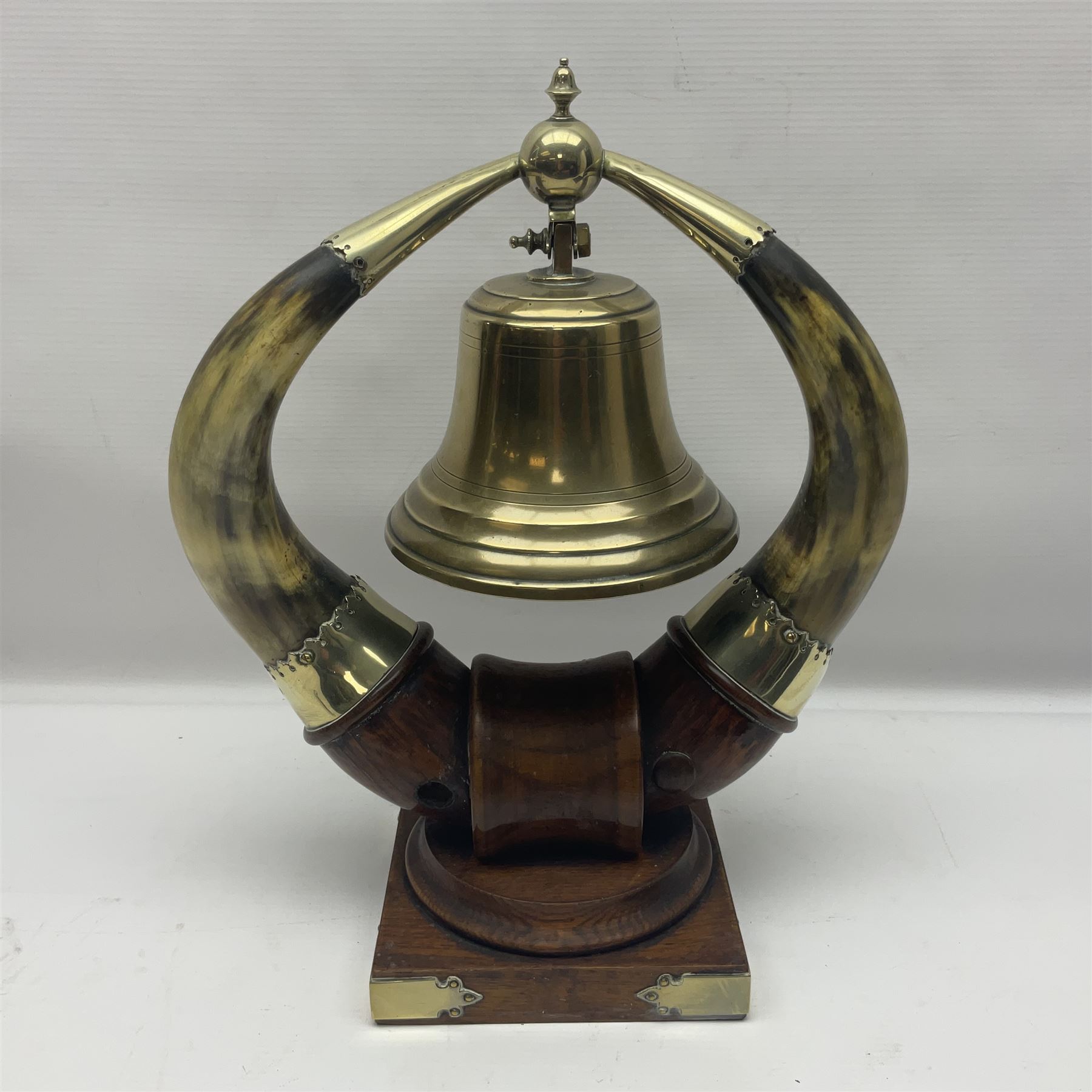 Early 20th century oak and horn dinner bell, the silvered bell suspended from a pair of cow horns, with silver plated mounts and blank shield shaped cartouche, upon square base, H37cm