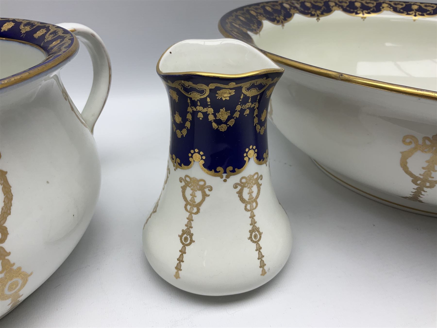 Early 20th century Bishop and Stonier four piece toilet set, comprising washbowl, wash jug, toothbrush pot, and chamber pot, each  decorated with deep blue band and husk swags and festoons in gilt, with printed Caduceus Bisto marks beneath and printed retailers mark 'Manufactured for Harrods Limited London', wash bowl D43cm, wash jug H31.5cm