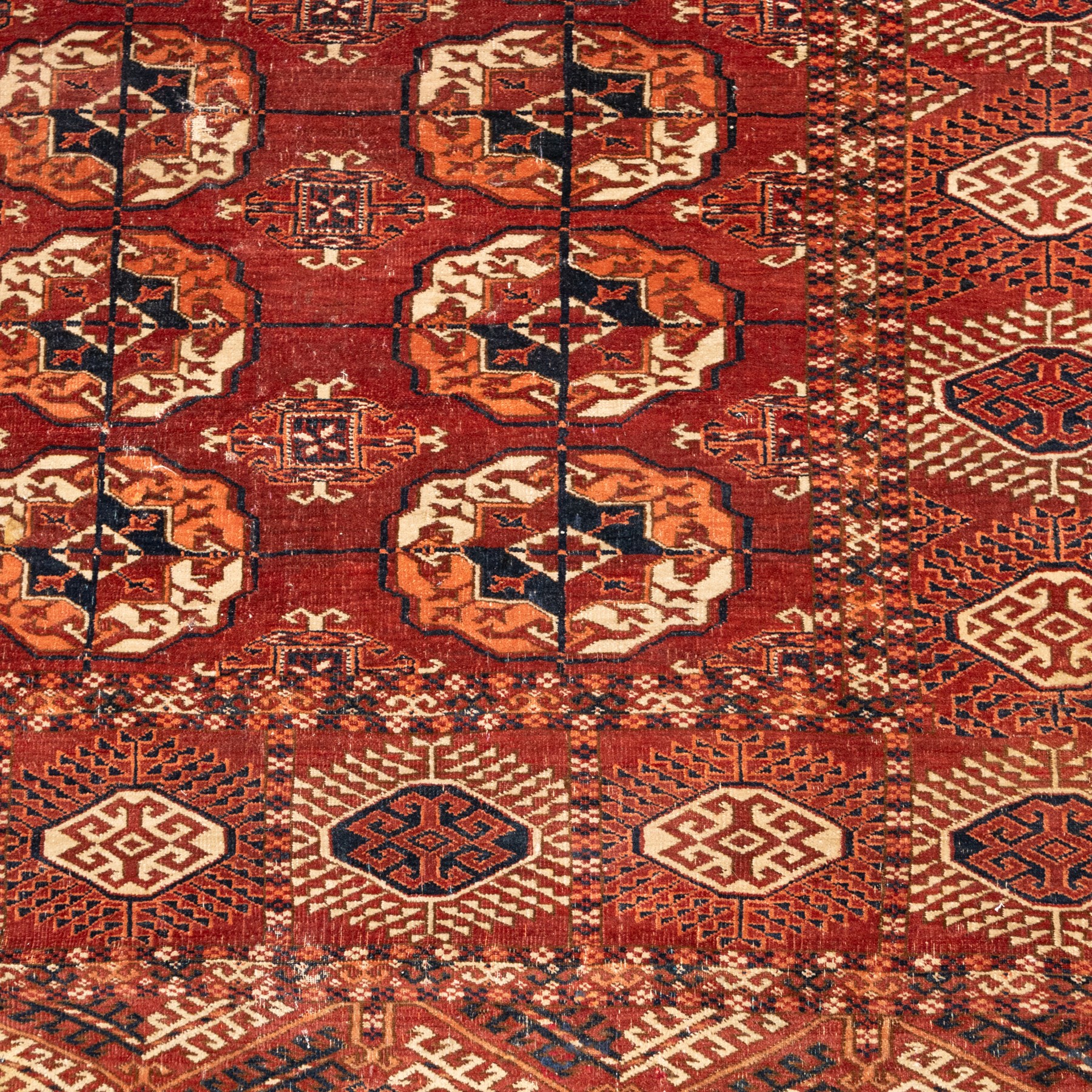 Persian Bokhara crimson ground rug, the field decorated with five rows of repeating Gul motifs with interspersed geometric design, enclosed by a guard band of further geometric-style Gul designs comprised of hook motifs