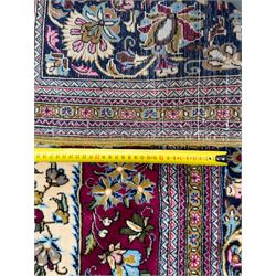 Central Persian Ghom hand-knotted rug, ivory field with scrolling vines, palmettes and flowerheads around a central lobbed medallion with pendants, framed by burgundy spandrels and a navy border of rosettes and arabesques, 289cm x 214cm