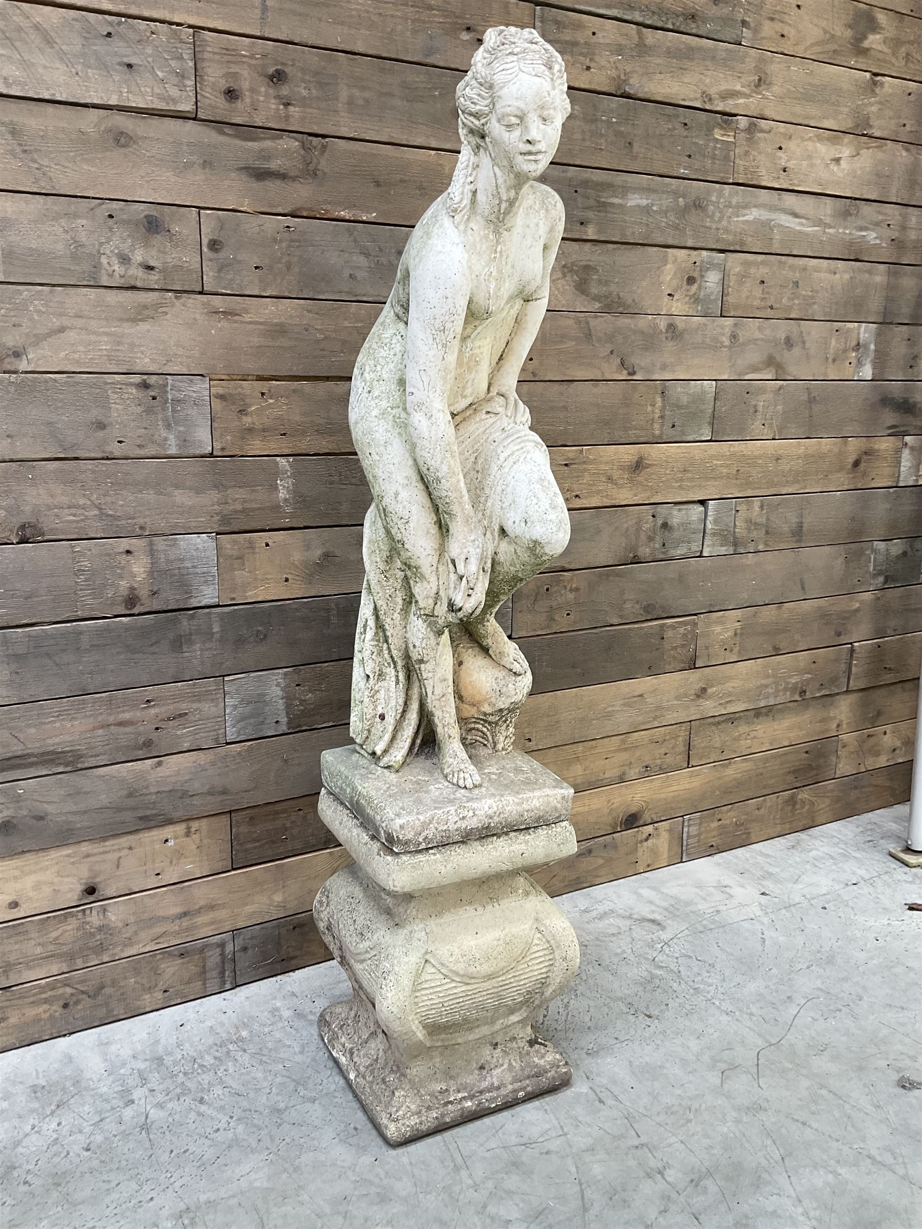 Cast stone garden statue of partially draped classical female figure on ornate pedestal 