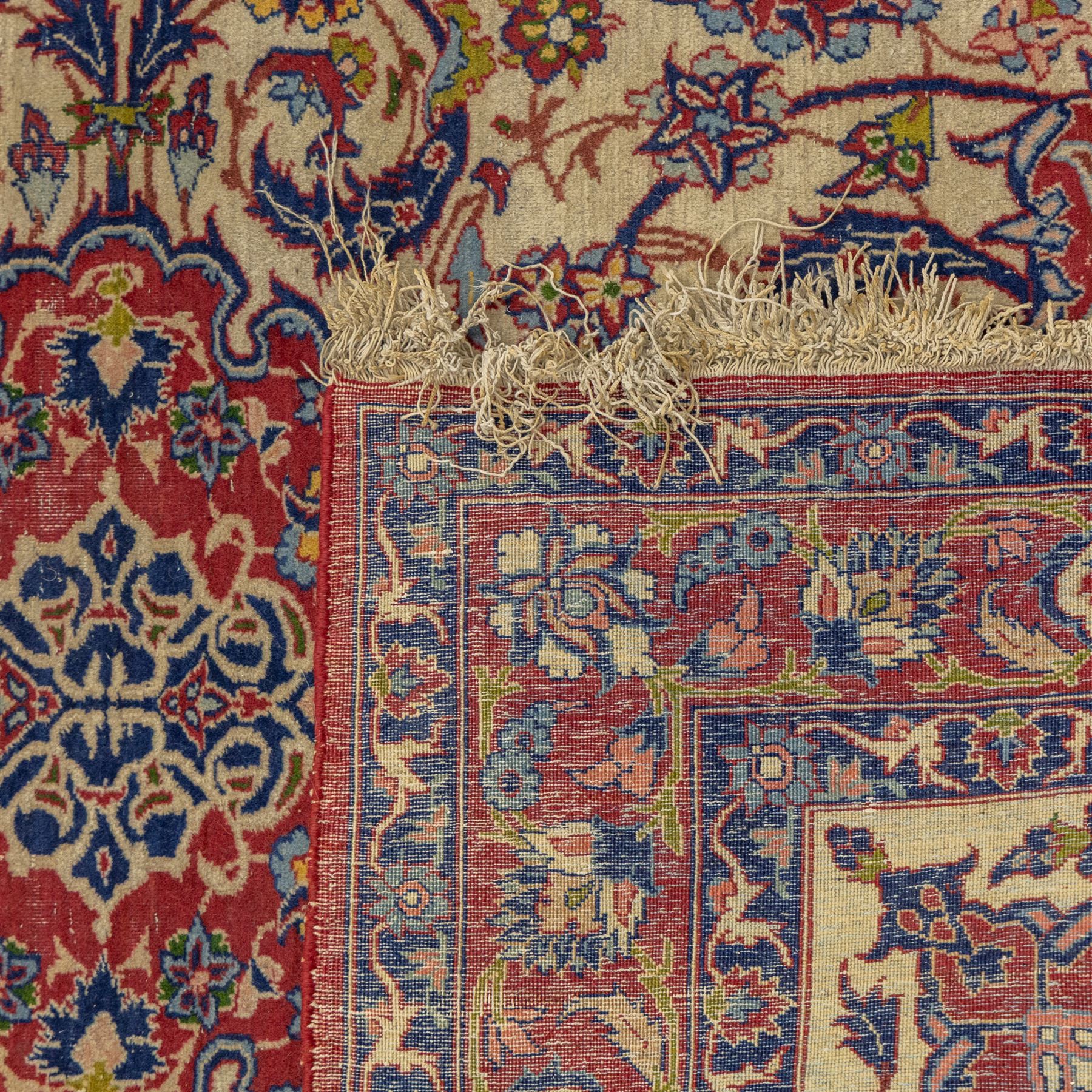 Kashan design wool rug, with red floral medallion on a cream field, decorated with scrolling foliate motifs in blue, red and green tones, enclosed by red and blue floral borders with fringed ends