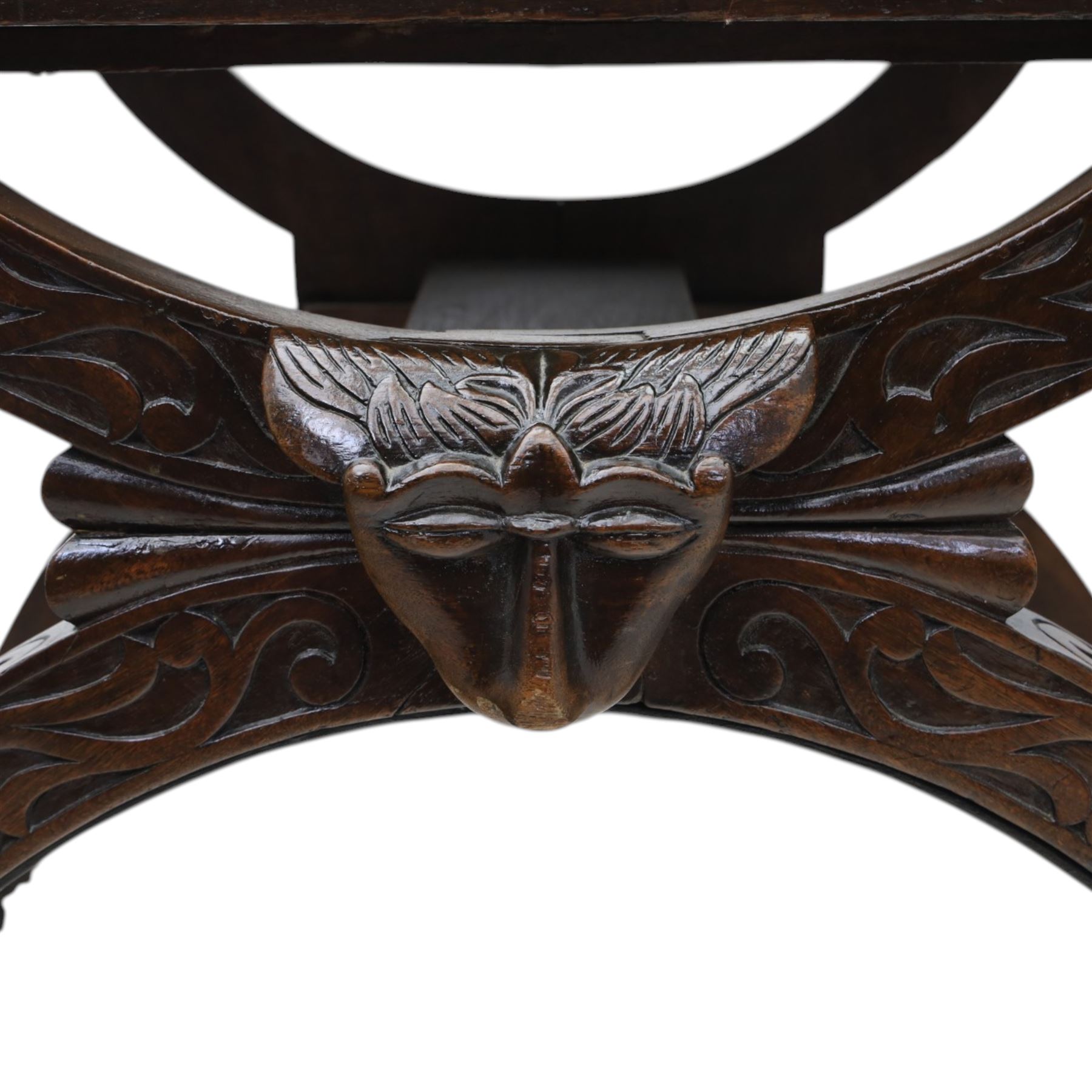 Late 20th century stained beech Savonarola chair, the carved crest rail and open arms above an upholstered leather seat, raised on an X framed base with carved foliate and mask decoration, joined by turned stretcher and ending in castors