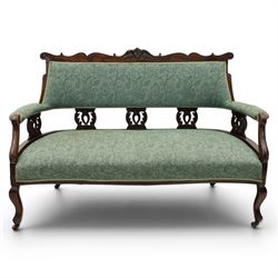 Edwardian mahogany framed sofa, shaped cresting rail with scroll terminals and carved foliate pediment, upholstered back and swept arms in green foliate fabric, pierced splat supports, serpentine front seat rail, on cabriole supports terminating in castors